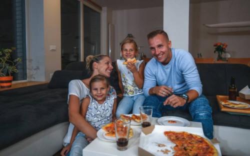 caucasian family sitting on a sofa eating pizza and watching tv - junk food stock pictures, royalty-free photos & images