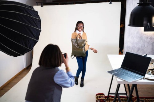 caucasian female photographer, taking photos of the female fashion model black ethnicity, while posing with an leather bag - fashion stock pictures, royalty-free photos & images