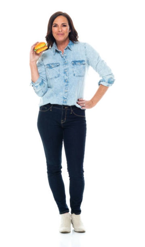 caucasian female standing in front of white background wearing jeans and holding bun - bread - junk food stock pictures, royalty-free photos & images