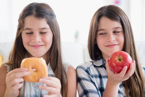caucasian twin sisters eating healthy and unhealthy snacks - junk food stock pictures, royalty-free photos & images