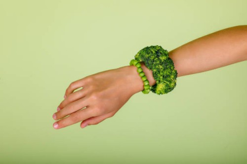 celebrating veganism: woman hand wearing a broccoli bracelet, symbolizing a commitment to a healthy lifestyle and unity with nature in green studio - fashion stock pictures, royalty-free photos & images