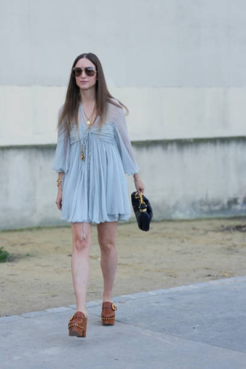 Charlotte Groeneveld wears dark brown sunglasses, gold layered Chloe necklaces, light blue sheer mesh short sleeve Chloe mini dress, gold bracelets,...