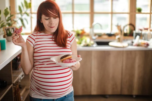 charming pregnant woman holding a plate with donughts and enjoyig her cravings - junk food stock pictures, royalty-free photos & images
