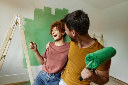 cheerful couple embracing while painting their new home. - home decoration stock pictures, royalty-free photos & images