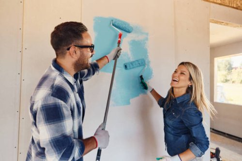 cheerful couple having fun while painting walls in the house. - home decoration stock pictures, royalty-free photos & images