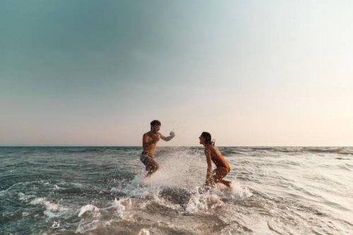 cheerful couple having fun while splashing each other at sea. - travel stock pictures, royalty-free photos & images