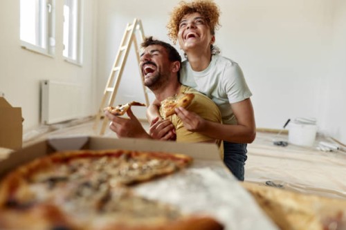 cheerful couple in love eating pizza on a break from home renovation process. - junk food stock pictures, royalty-free photos & images
