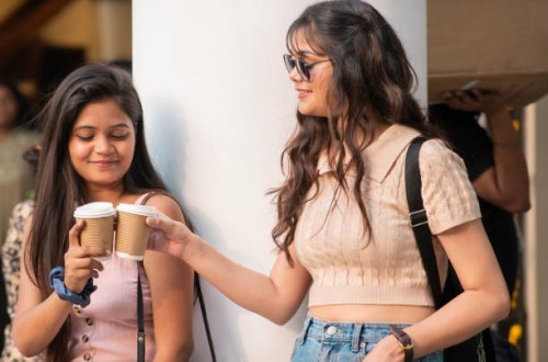 cheerful female friends enjoying coffee takeaway while walking on city street - junk food stock pictures, royalty-free photos & images