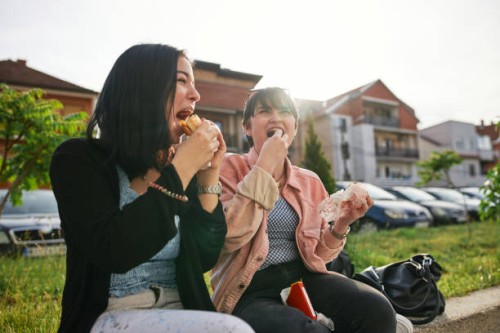 cheerful hipster friends eating fast food outdoors - junk food stock pictures, royalty-free photos & images