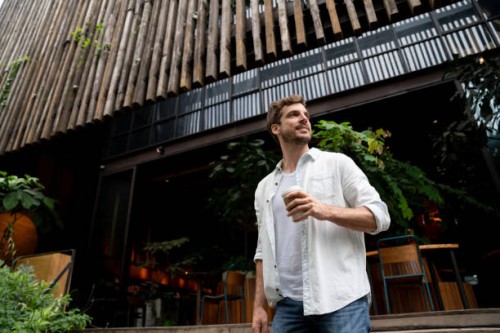 cheerful latin american guy leaving a coffee shop looking away smiling - junk food stock pictures, royalty-free photos & images