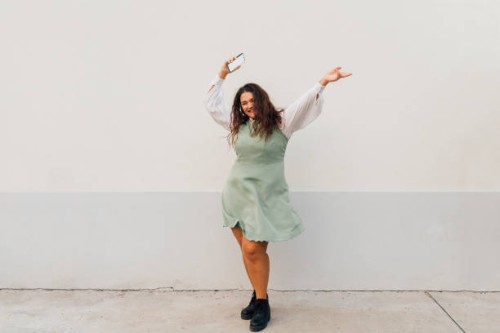 cheerful plus size woman with smart phone dancing against wall - fashion stock pictures, royalty-free photos & images