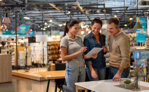 cheerful sales woman showing a design on tablet to mid adult couple looking for furniture at a home store - home decoration stock pictures, royalty-free photos & images