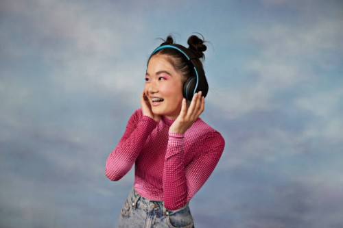 cheerful teenage girl listening to music through wireless headphones against colored background - fashion stock pictures, royalty-free photos & images