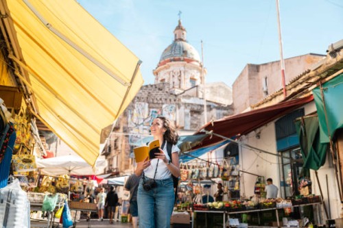 cheerful tourist reading a travel guide in ballarò market, palermo, sicily, italy - travel photos et images de collection