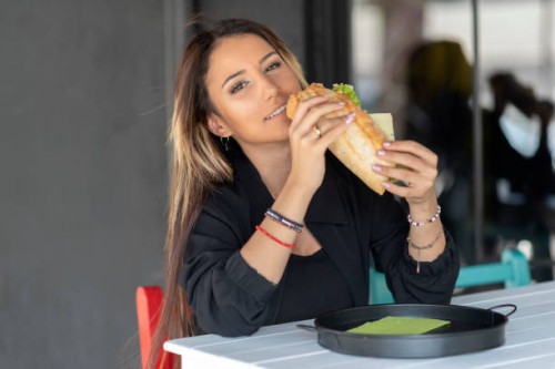 cheerful woman eating a sandwich - junk food stock pictures, royalty-free photos & images