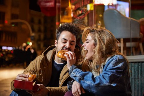 cheerful woman feeding burger to man at night - junk food stock pictures, royalty-free photos & images