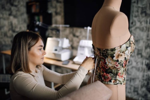 cheerful young female designer ties ribbons on captivating corset put on dressmaker model - fashion stock pictures, royalty-free photos & images