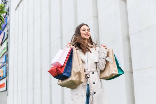 cheerful young lady dancing with colorful shopping bags while standing outdoors. happy dark haired woman enjoying successful shopping during black friday. - fashion stock pictures, royalty-free photos & images