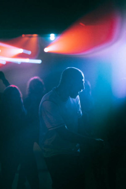 cheerful young man dancing against illuminated spotlight at nightclub - concert stock pictures, royalty-free photos & images