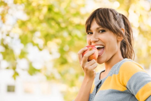 cheerful young woman eating an apple - food stock pictures, royalty-free photos & images