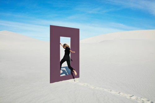 cheerful young woman jumping through door frame at desert - fashion stock pictures, royalty-free photos & images