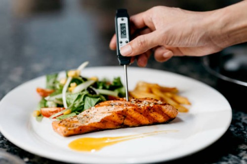 chef utilise un thermomètre pour mesurer la température du filet de saumon poêlé - food photos et images de collection