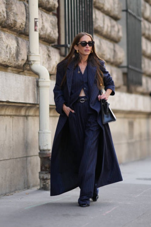 Chloe Harrouche wears sunglasses, a navy blue striped long trench coat, a waistcoat, matching flared suit pants, outside Hermes, during the...