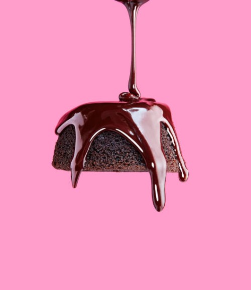 chocolate frosting being poured onto chocolate cake with pink background - food stock pictures, royalty-free photos & images