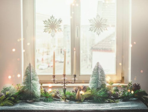 christmas home decoration with candlestick, christmas trees, fir green and pine cones on table with table cloth at window background with hanging snowflakes - home decoration stock pictures, royalty-free photos & images
