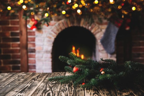christmas tree branch on a wooden table against the background of a fireplace, place for text, christmas concept, christmas toys and blurry lights - home decoration stock pictures, royalty-free photos & images
