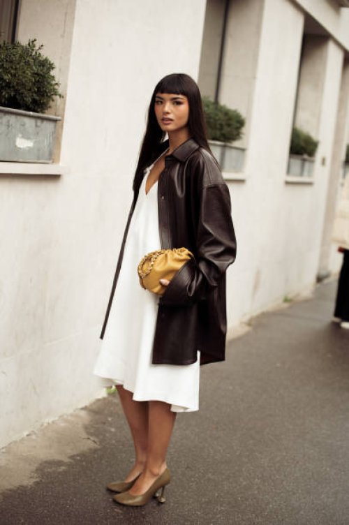 Clara Kong Vila wears white dress, brown high heels, black leather jacket and yellow bag outside the LOEWE presentation during the Womenswear...
