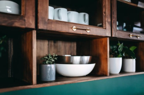 classic kitchen interior with brown coloured wooden cabinets and shelves against dark green coloured wall. crockery, dishes and houseplants on the shelves - home decoration stockfoto's en -beelden