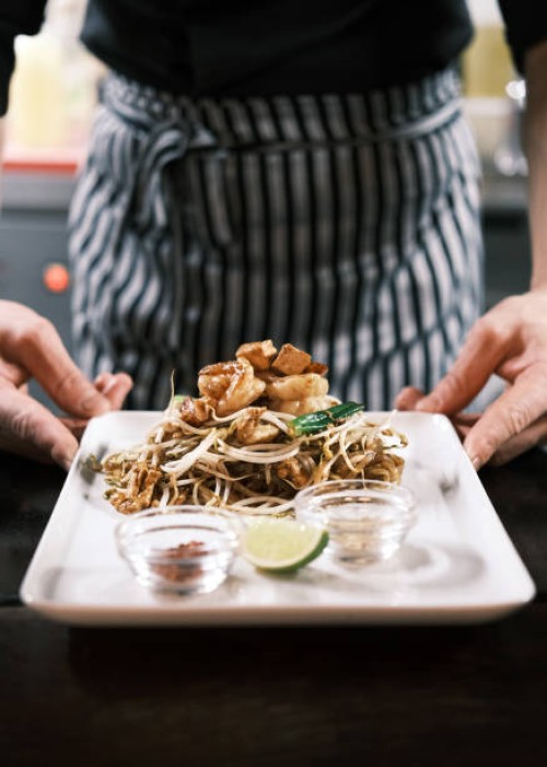 classic thai pad thai noodles with stir-fried shrimp, fresh vegetables, lime, and condiments elegantly presented on a white plate in a traditional restaurant setting - junk food stock pictures, royalty-free photos & images