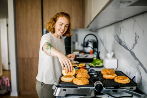 close-up of a woman toasting burger buns on an electric home grill in the kitchen. - junk food stock pictures, royalty-free photos & images