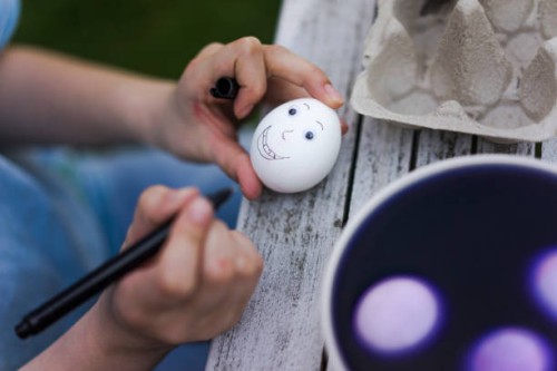 close-up of girl painting face on easter egg on garden table - garden decoration stock-fotos und bilder