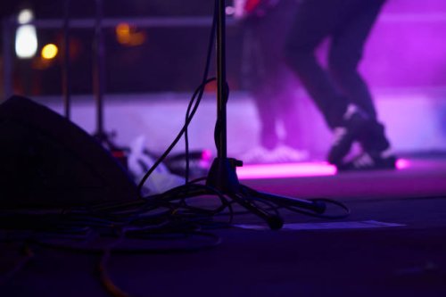 close-up of low section of a microphone stand with musicians playing on the background on a lighted stage during a music concert at night - concert stock pictures, royalty-free photos & images