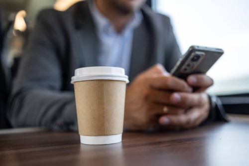 close-up of takeaway coffee on desk with businessman using smartphone - junk food stock pictures, royalty-free photos & images