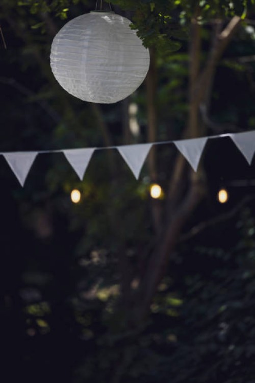 close-up of white flag garland and paper lantern against trees. garden party, summer festival, birthday party, baptism or wedding. - garden decoration stockfoto's en -beelden