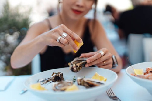 close-up of woman's hand squeezing lemon juice on fresh oysters - food stock pictures, royalty-free photos & images