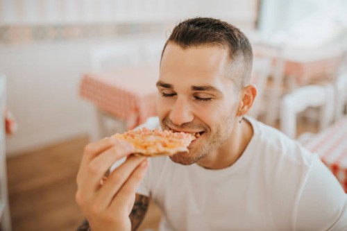 close-up of young man with eyes closed eating pizza while sitting in restaurant - junk food stock pictures, royalty-free photos & images