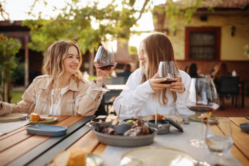 close-up portrait of two female friends in strict suits laughing drinking wine on the terrace outside at summer street cafe - food stock pictures, royalty-free photos & images