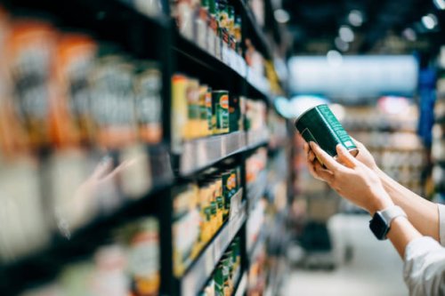 close up of a woman grocery shopping in supermarket. holding a tin can and reading the nutrition label at the back - junk food stock pictures, royalty-free photos & images