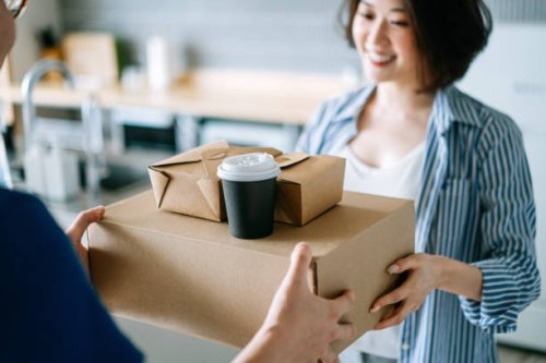 close up of beautiful and cheerful young asian woman receiving home delivery takeaway food order from a delivery man at home. eating at home concept - junk food stock pictures, royalty-free photos & images
