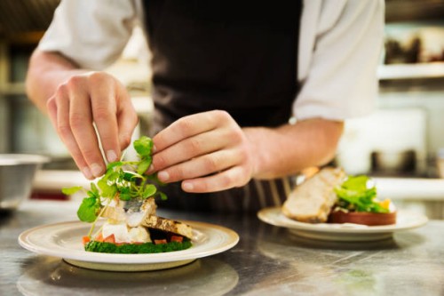 close up of chef in kitchen adding salad garnish to a plate with grilled fish. - food stock pictures, royalty-free photos & images