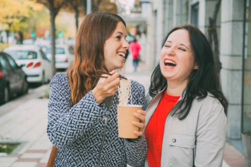 close up of two caucasian young women laughing in the street while eating asian food. food concept - junk food stock pictures, royalty-free photos & images