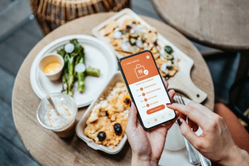 close up of woman's hand ordering home delivery takeaway food with mobile app on smartphone, tracking status and confirming food order. enjoying nachos, baked mac and cheese and baby broccoli in the balcony at home. technolog