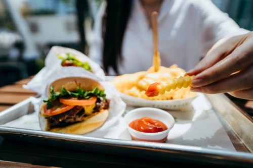close up of young asian woman dipping fries with ketchup and eating beef burger in an outdoor fast food restaurant - junk food stock pictures, royalty-free photos & images