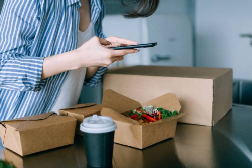 close up of young asian woman standing by the kitchen counter, taking a photo of delicious home delivery takeaway lunch box of fresh healthy salad with smartphone, sharing on social media before eating it. eating at home conc