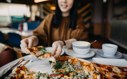 close up of young woman enjoying meal and eating freshly made pizza in a restaurant - junk food stock pictures, royalty-free photos & images