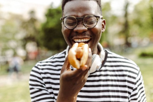 close up portrait of young man eating hot dog outdoors - junk food stock pictures, royalty-free photos & images